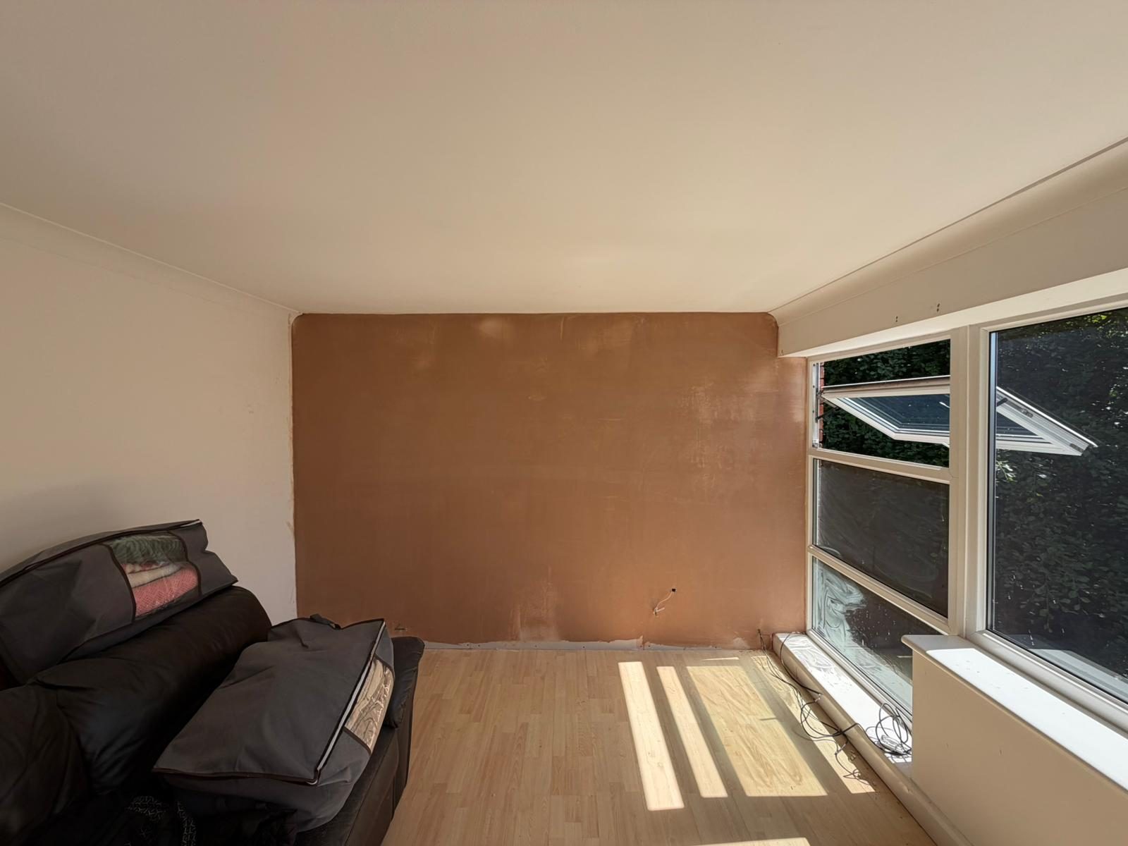 Fresh plaster skim over insulated lounge wall — pink finish ready to dry out